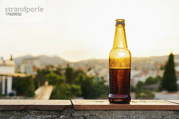 Bierflasche auf Stützmauer bei Sonnenuntergang