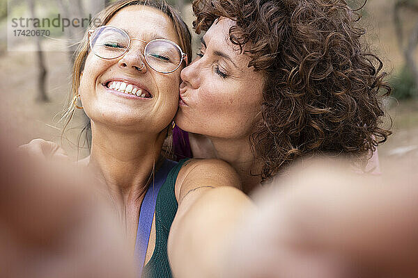 Lächelnde Frau macht Selfie mit Freund  der sich auf die Wange küsst