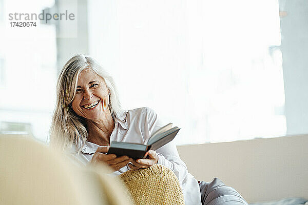 Glückliche reife Frau  die mit einem Buch auf einem Stuhl im Café sitzt