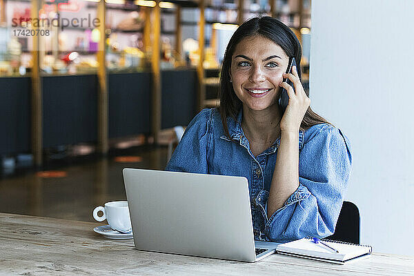 Lächelnde junge Geschäftsfrau  die im Café mit dem Handy telefoniert