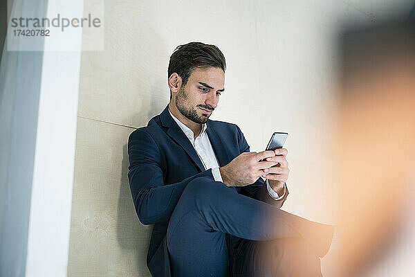 Junger Geschäftsmann schreibt Textnachrichten per Smartphone  während er im Büro sitzt