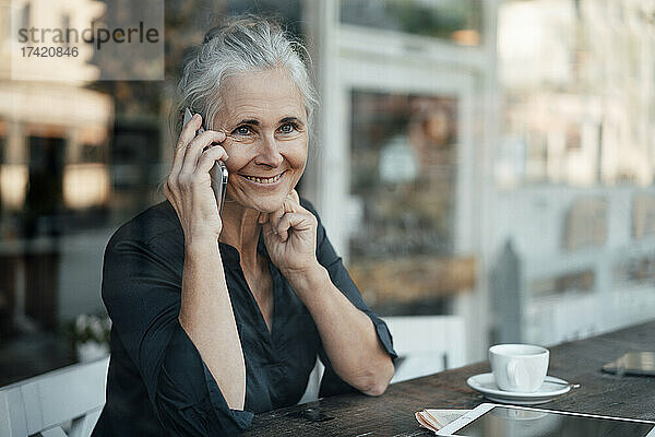 Lächelnde reife Geschäftsfrau  die im Café mit dem Handy spricht