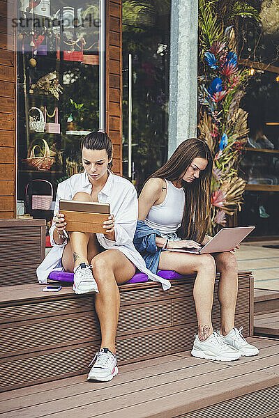 Freundinnen nutzen digitales Tablet und Laptop auf der Bank