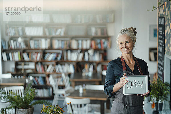 Lächelnde Cafébesitzerin hält digitales Tablet mit offenem Text im Café