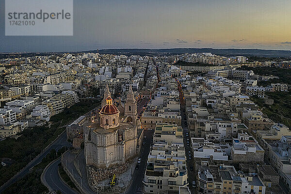 Malta  Nordregion  Mellieha  Luftaufnahme der Stadt in der Abenddämmerung mit der Pfarrkirche der Geburt der Jungfrau Maria im Vordergrund