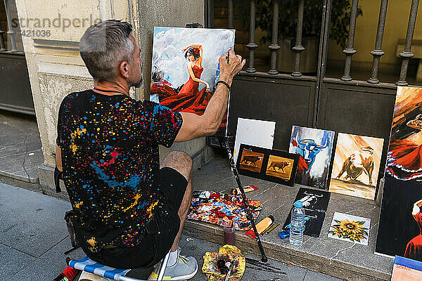 Männlicher Künstler malt Frau  während er auf dem Fußweg sitzt