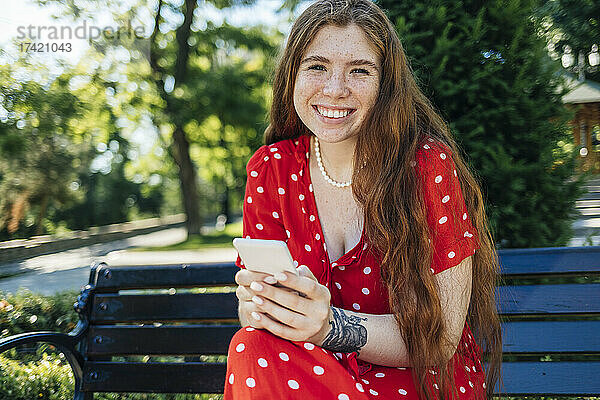 Frau hält Smartphone in der Hand  während sie im Sommer im Park sitzt