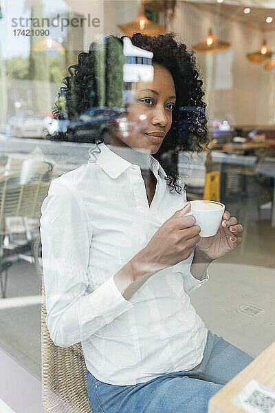 Nachdenkliche Geschäftsfrau mit Kaffeetasse  die durch das Caféfenster schaut