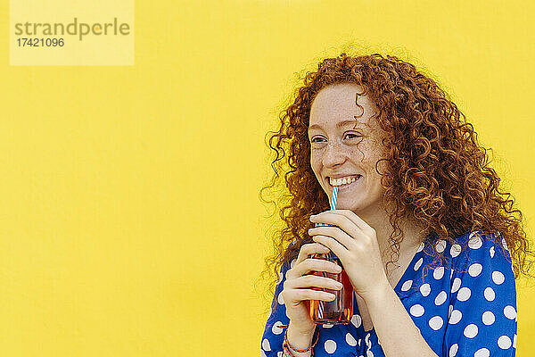 Lächelnde Frau trinkt Saft vor gelber Wand