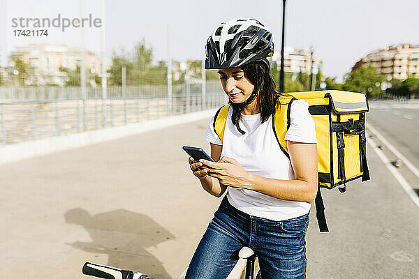 Weibliche Zustellerin mit Fahrrad und Mobiltelefon an sonnigem Tag