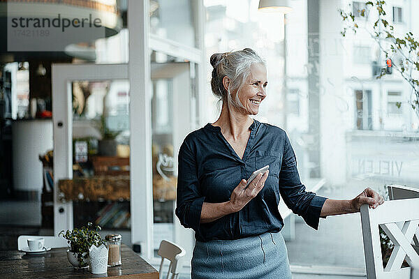 Geschäftsfrau mit Mobiltelefon steht am Cafétisch