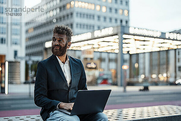 Geschäftsmann mit Laptop sitzt auf Bank am Bahnhof