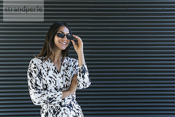 Lächelnde junge Frau mit Sonnenbrille vor schwarzer Wand