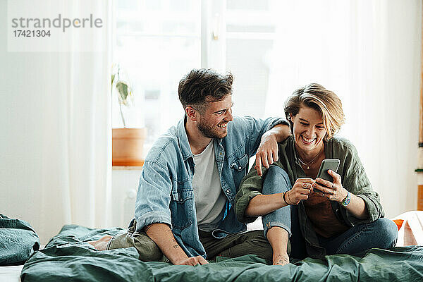 Mann sitzt mit Frau und benutzt Smartphone zu Hause im Bett
