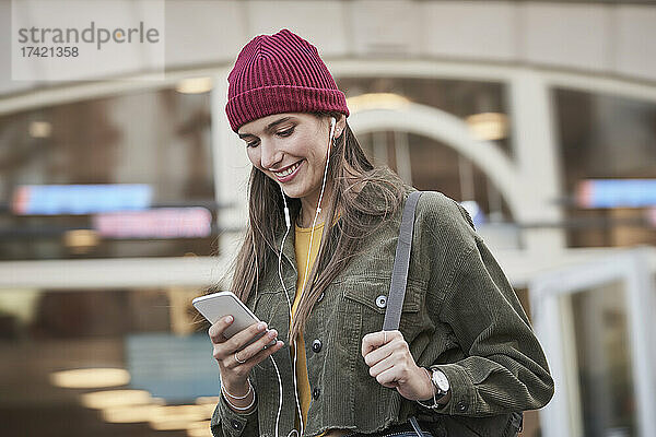 Lächelnde junge Frau  die vor dem Gebäude ihr Mobiltelefon benutzt