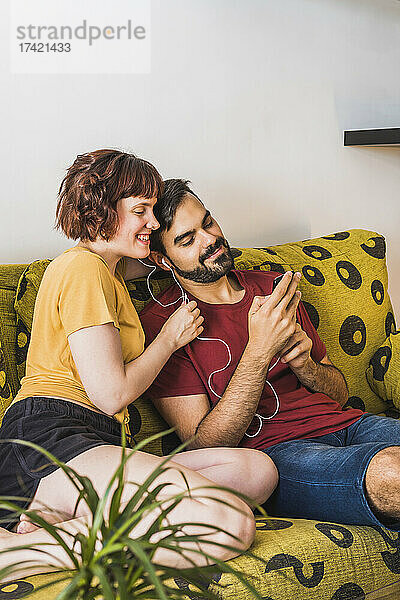 Junger Mann zeigt Freundin auf Sofa Handy