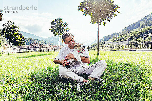 Mitte erwachsener Mann mit Hund sitzt im Schneidersitz auf Gras
