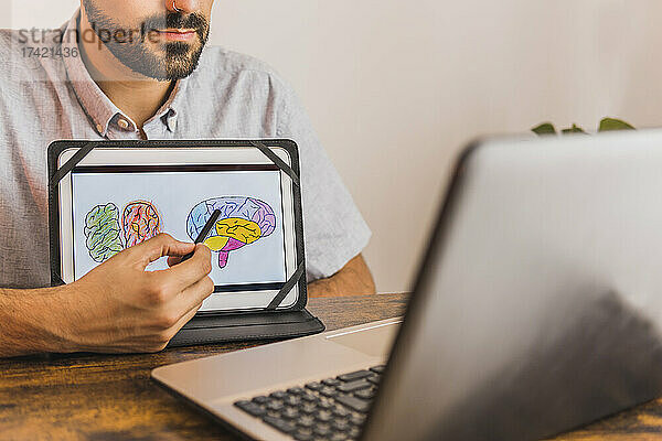 Männlicher Psychiater zeigt während der Online-Therapie ein Gehirndiagramm auf einem digitalen Tablet