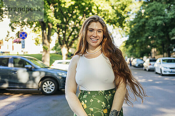 Lächelnde Frau mit langen Haaren steht auf der Straße