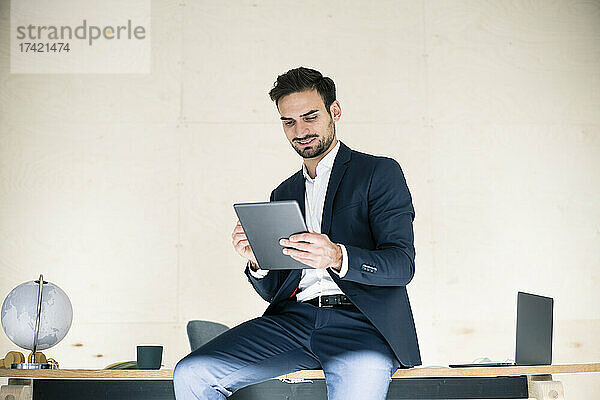 Junger männlicher Berufstätiger nutzt digitales Tablet  während er am Schreibtisch im Büro sitzt