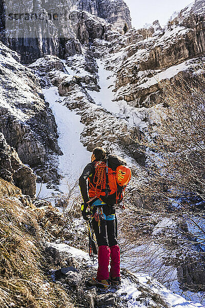 Männlicher Wanderer blickt auf den Berg  während er auf einem Felsen steht  Bergamasker Alpen  Lecco  Italien