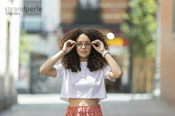 Junge Frau mit Brille inmitten von Gebäuden an einem sonnigen Tag