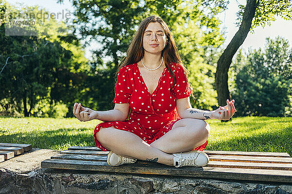Frau meditiert  während sie mit gekreuzten Beinen auf einer Bank sitzt