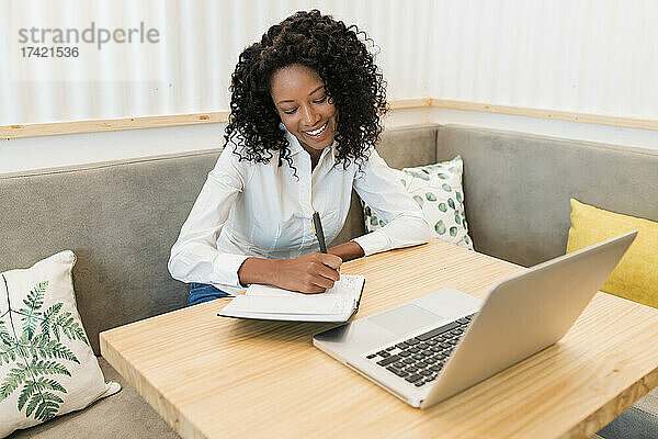 Lächelnde Geschäftsfrau schreibt in ein Buch  während sie im Café sitzt