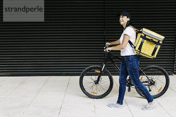 Lächelnde Lieferfrau  die mit dem Fahrrad auf dem Fußweg läuft