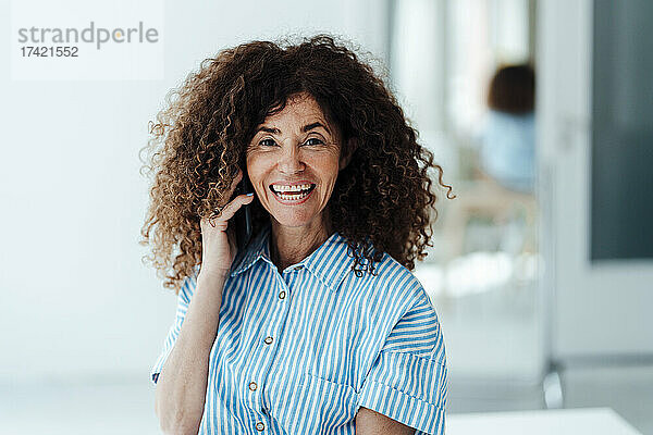 Lächelnde Geschäftsfrau  die im Büro mit dem Mobiltelefon spricht