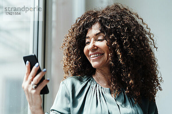 Geschäftsfrau mit lockigem Haar nutzt Smartphone im Büro