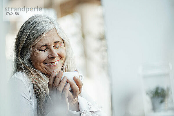 Lächelnde Frau mit geschlossenen Augen hält Kaffeetasse im Café