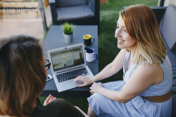 Eine berufstätige Frau diskutiert mit einer Kollegin  während sie mit einem Laptop auf dem Dach sitzt