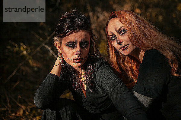 Freunde mit Halloween-Make-up und Kostüm sitzen im Wald