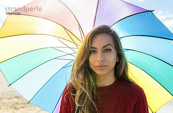 Lächelnde Frau mittleren Alters mit buntem Regenschirm an einem sonnigen Tag