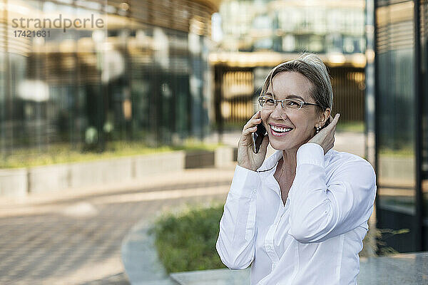 Fröhliche Geschäftsfrau mit der Hand im Haar  die mit dem Handy spricht