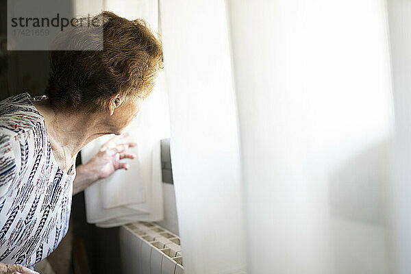 Ältere Frau schaut zu Hause durch das Fenster