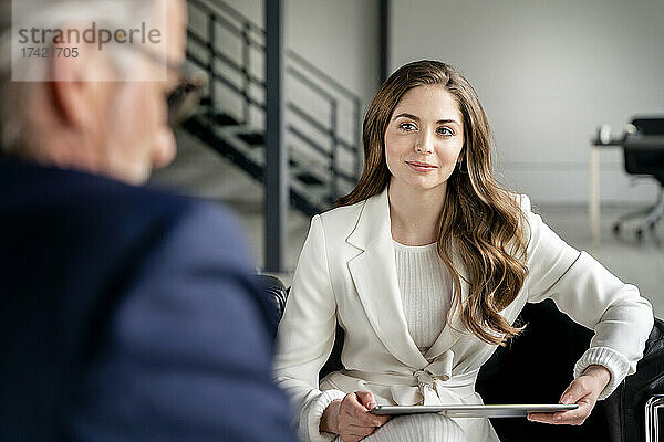 Schöne Geschäftsfrau mit digitalem Tablet blickt auf männlichen Berufstätigen im Büro