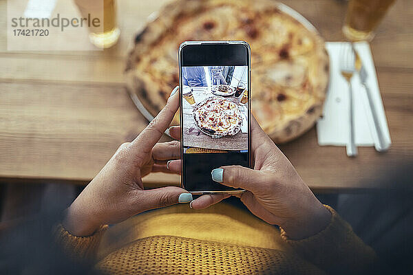 Junge Frau fotografiert Pizza per Smartphone