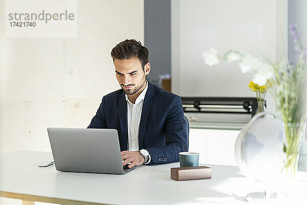 Junger Geschäftsmann benutzt Laptop  während er am Schreibtisch im Büro sitzt