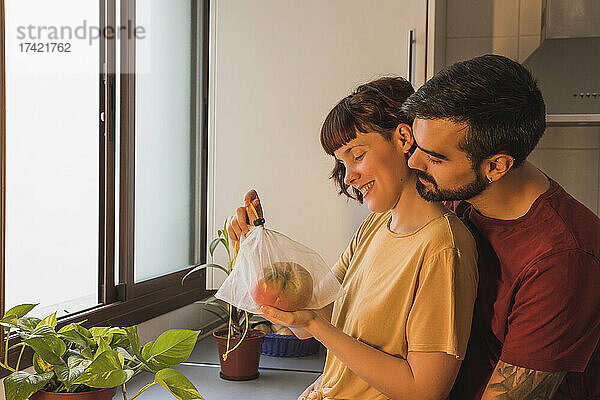 Mann umarmt Freundin und hält Beefsteak-Tomate in der heimischen Küche