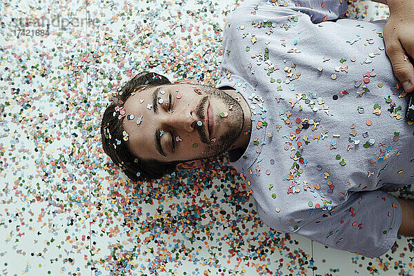 Man's face covered with confetti relaxing on floor