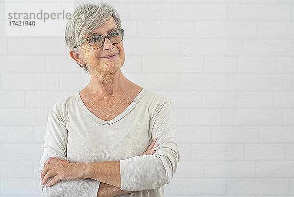 Lächelnde ältere Frau  die im Stehen mit verschränkten Armen nachdenkt