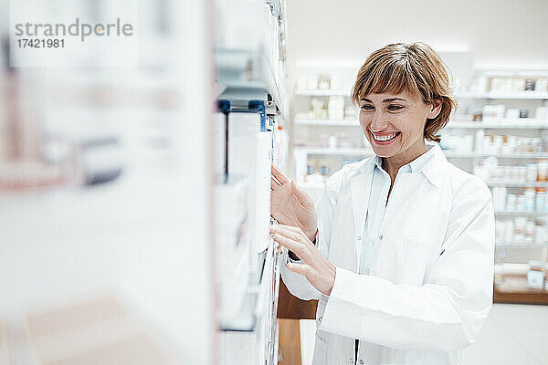 Lächelnde Apothekerin im Laborkittel sucht in der Apotheke nach Medikamenten
