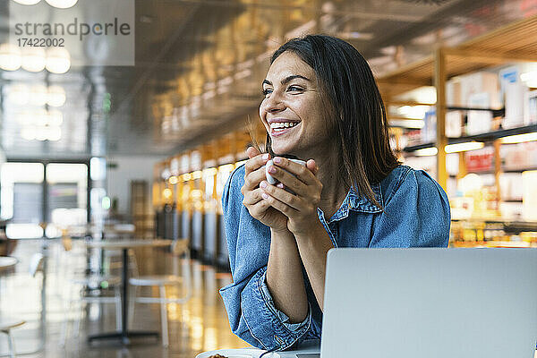 Glückliche Geschäftsfrau mit Laptop beim Kaffee im Café