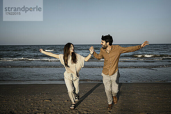 Fröhliches Paar hält Händchen beim Laufen am Strand