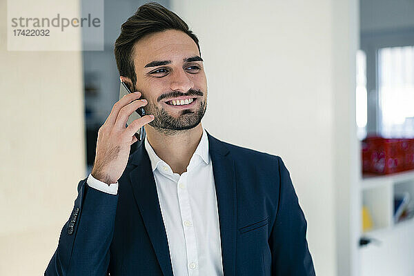 Glücklicher männlicher Berufstätiger  der im Büro auf dem Smartphone spricht