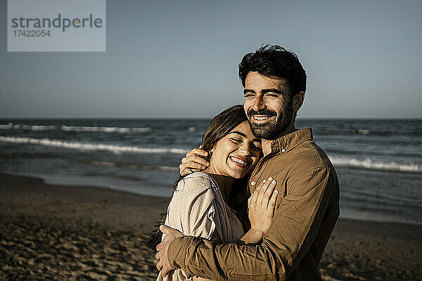 Glückliches junges Paar umarmt sich  während es am Strand steht