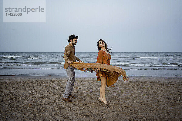 Paar spielt im Urlaub mit Decke am Strand