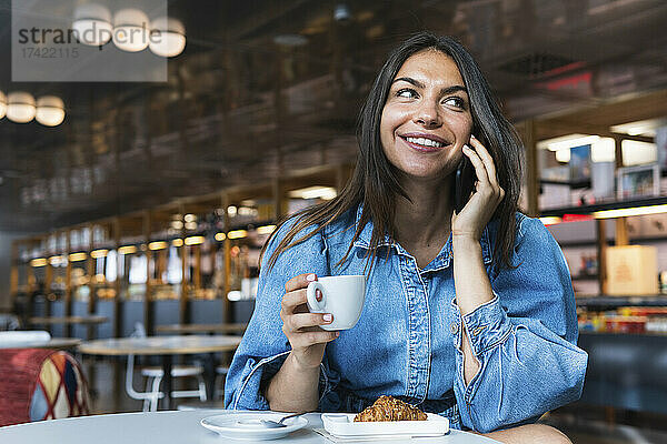 Geschäftsfrau mit Kaffeetasse lächelt  während sie im Café mit dem Smartphone spricht